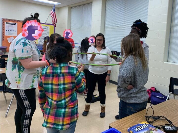 College student mentors and middle school youth in an after school club work together to hold a hula hoop level usng only one finger per person