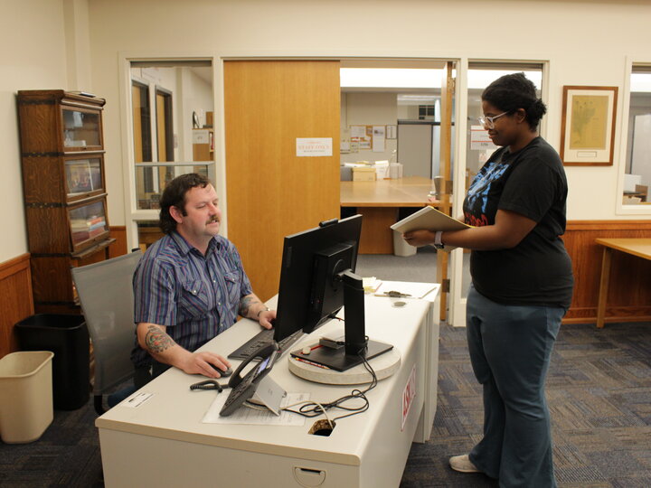 Archives staff helping a patron at the front desk with finding materials